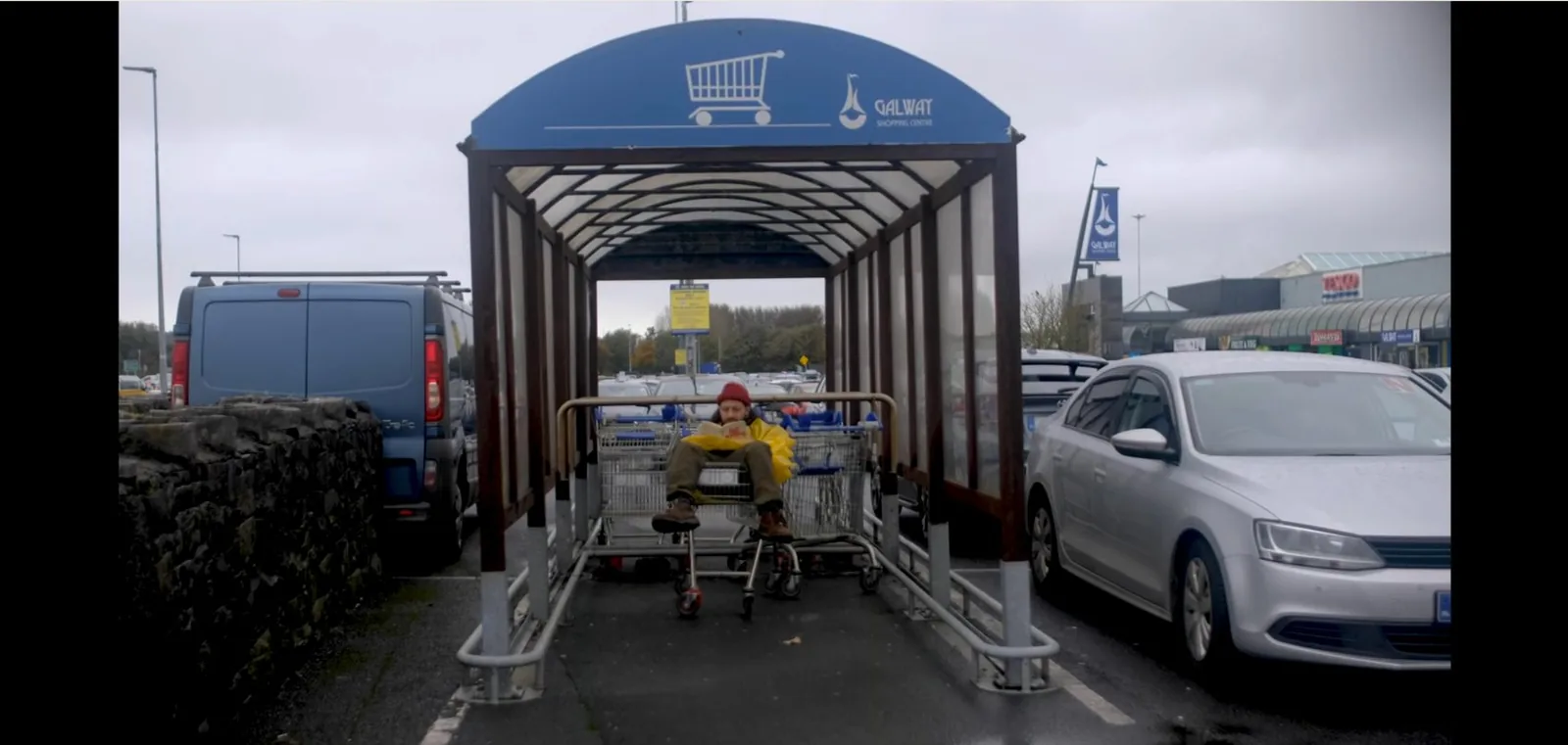 Still from the film, reading in a shopping-trolley shelter, Galway