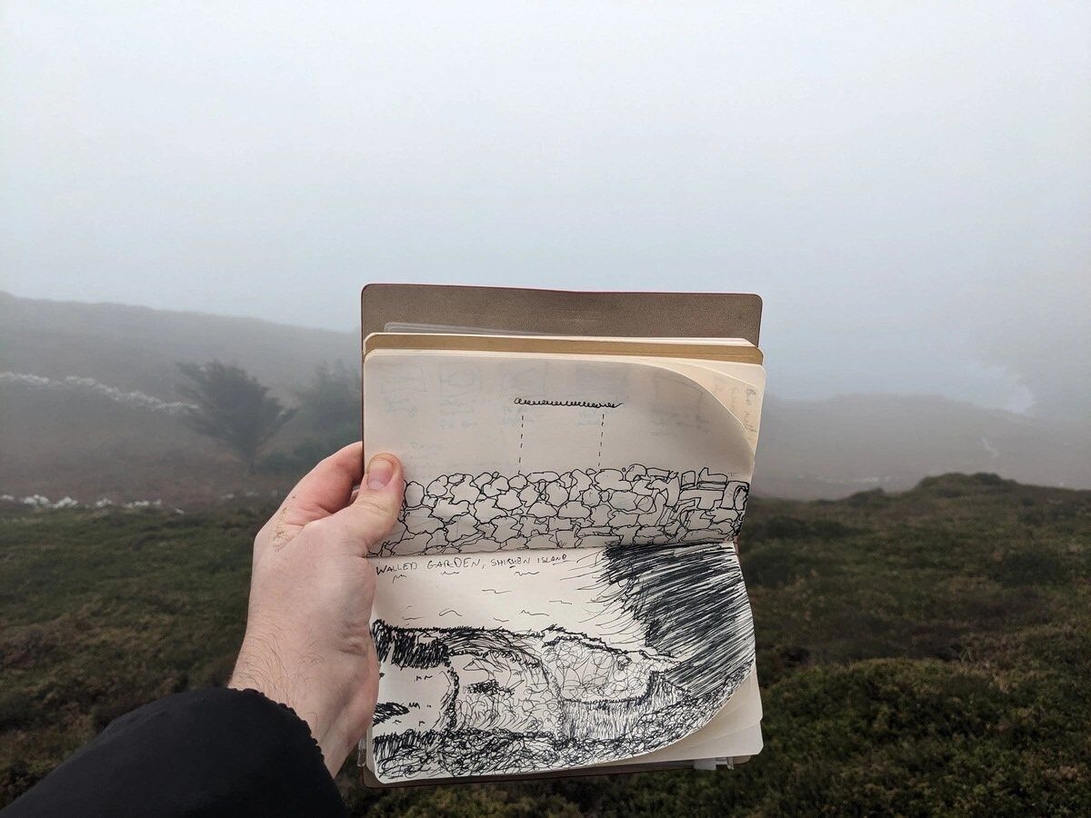 A hand holding an open sketchbook with Walled Garden, Sherkin Island notes